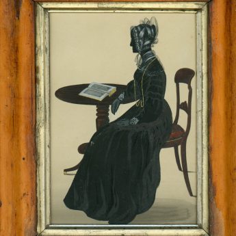 Painted and gilded silhouette of a lady seated at a table with an open book